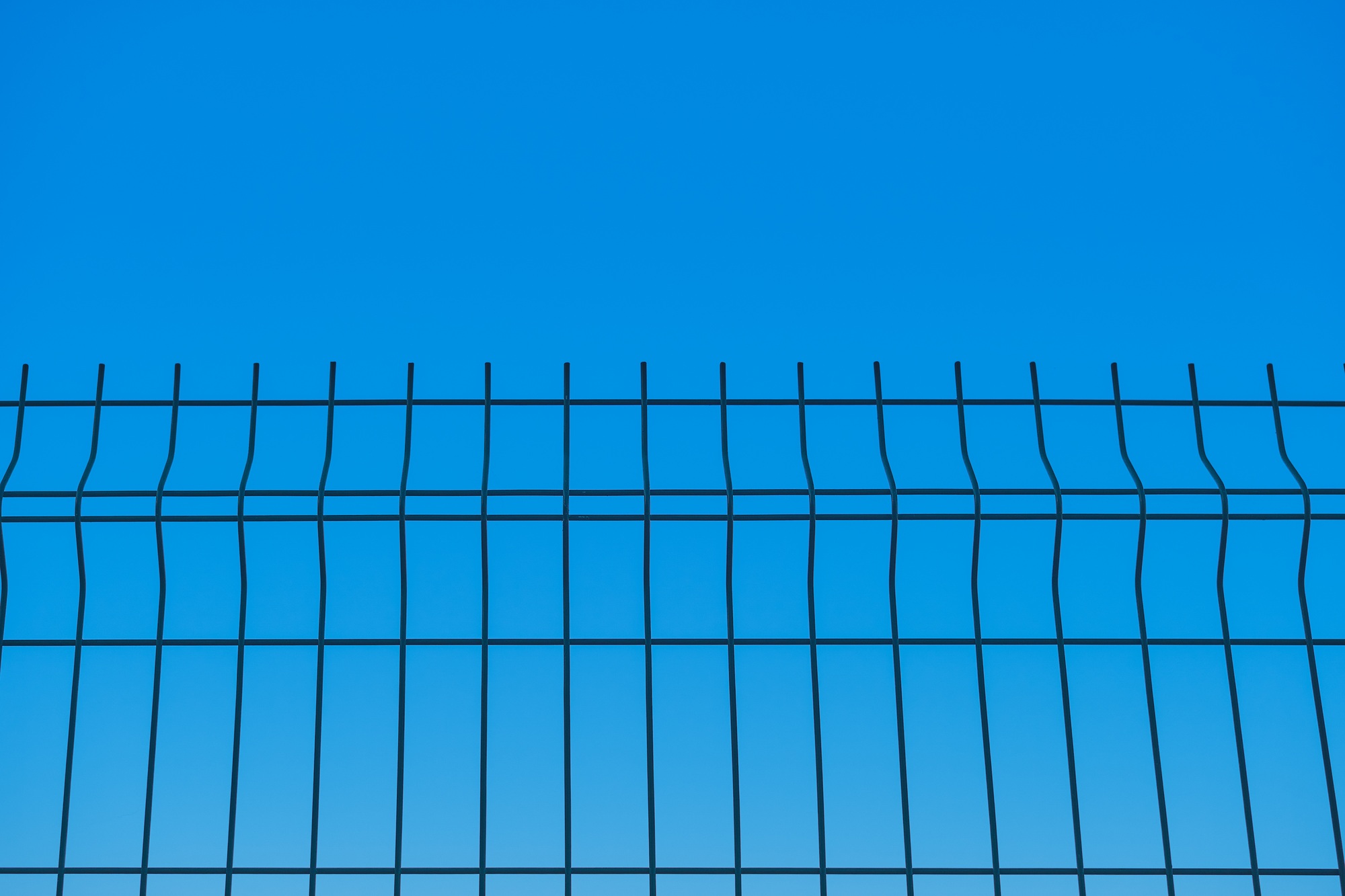Metal fence against the background of a blue boundless sky